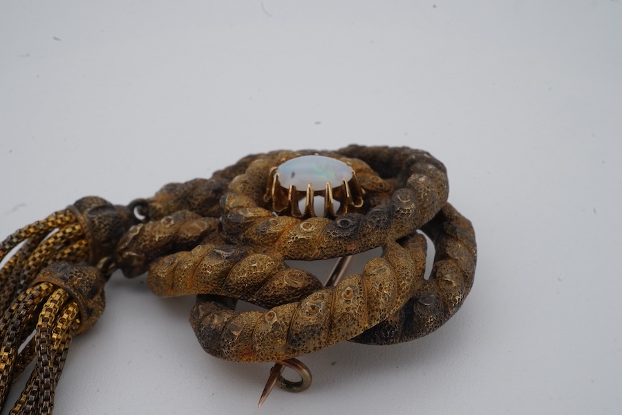 A Victorian opal brooch, mid 19th century, of knotted design in textured gold, set with a cabochon opal, suspending two tassels, length 7cm, gross weight 14 grams